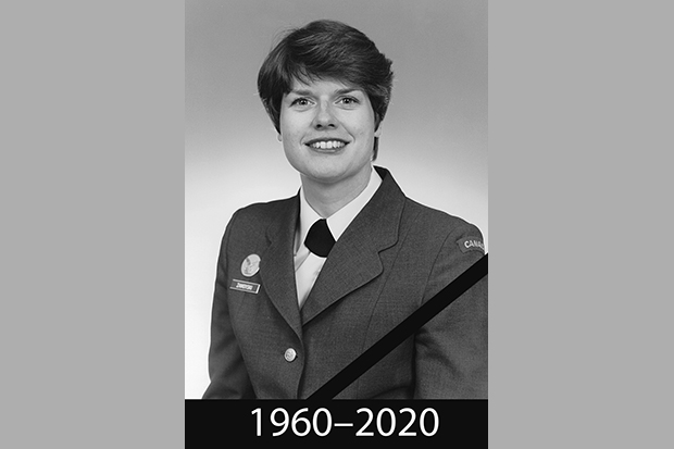 Czarno-biała fotografia en face młodej kobiety ubranej w wojskowy, galowy mundur. Włosy ciemne, krótko obcięte, oczy ciemne, uśmiecha się szeroko. Poniżej napis: 1960-2020.