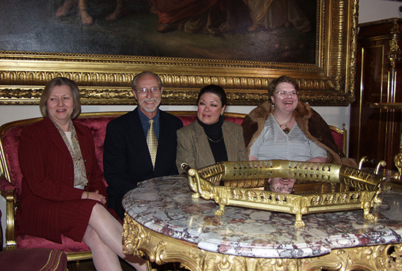 Fotografia. Cztery osoby, 3 kobiety i mężczyzna, ubrani elegancko, siedzą za stołem. Wszyscy uśmiechnięci.