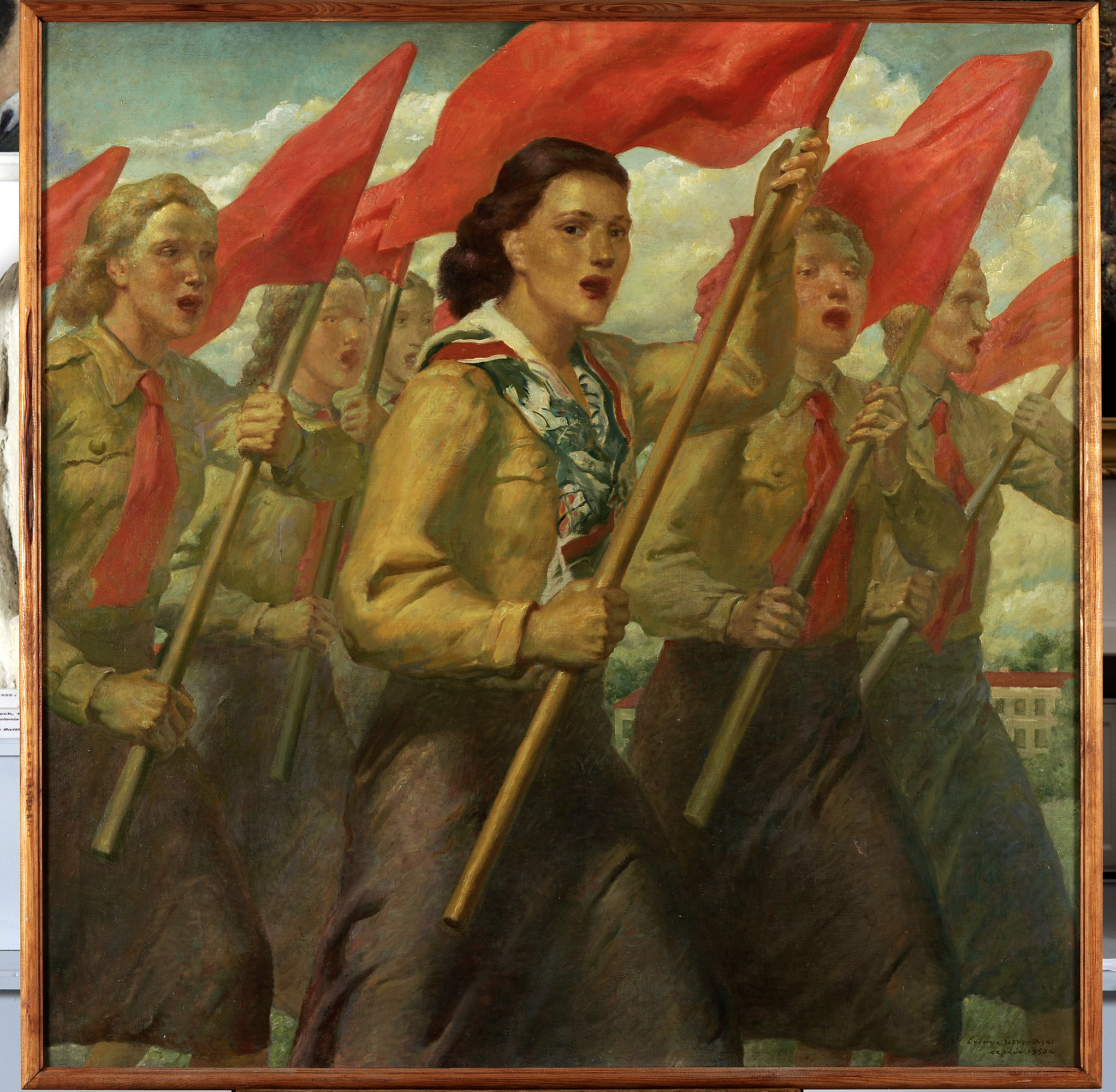 Obraz namalowany farbami olejnymi na płótnie z 1950 roku, autorstwa Ludomira Śledzińskiego, zatytułowany Wolny śpiew. Sześć dziewcząt maszerujących z czerwonymi flagami, ma usta rozchylone do śpiewu. Ubrane są w stroje organizacji Związku Młodzieży Polskiej, mają czerwone krawaty, jasne brązowo-zielone bluzy, spódnice ciemniejsze brązowe przechodzące w zieleń i fiolet. Dziewczyna w centrum kompozycji ma kasztanowe falujące włosy, zamiast krawata ma wzorzystą apaszkę z wzorem gołąbka pokoju. Pozostałe manifestantki to blondynki. W tle budynek z czerwonym dachem wśród zieleni i szarobłękitne, lekko zachmurzone niebo.