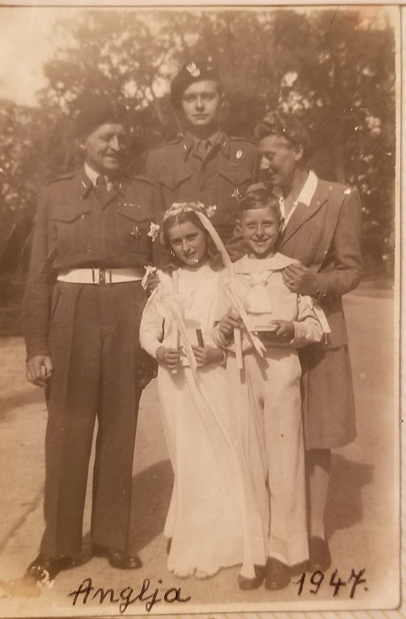 Fotografia archiwalna w sepii, zrobiona w 1947 roku. Przedstawia rodzinę Zamoyskich: pierwszy z lewej mężczyzna w średnim wieku, obok niego, nieco z tyłu wysoki, młody mężczyzna -obaj ubrani w mundury 2 Korpusu Polskiego. Dalej kobieta w średnim wieku, ubrana w białą bluzkę z kołnierzem, marynarkę i spódnicę. Kobieta obejmuje dłońmi dwoje dzieci stojących z przodu – dziewczynkę i chłopca – w białych strojach „komunijnych” – dziewczynka ma długą sukienkę i wianek z kwiatów i wstążek na głowie, chłopiec spodnie i bluzę o marynarskim kroju; w rękach trzymają białe, długie świece i małe książeczki. U dołu odręczny napisy „Anglia” i „1947”. W tle wysokie drzewa i fragment szerokiej drogi.