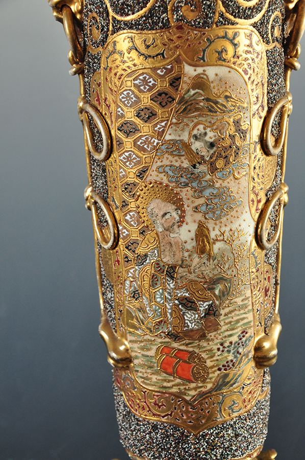 Na ceramicznym korpusie lampy naftowej bogato dekorowana złoceniami przestrzeń. W polu scena ukazująca klęczącego mężczyznę trzymającego złoty przedmiot w dłoni, nad nim z chmur wyłania się pochylona w jego kierunku w popiersiu postać kobieca.