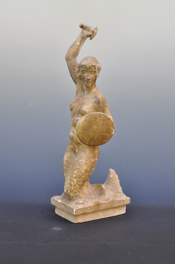 3.	Na zdjęciu model odlewniczy z gipsu, zatytułowany Warszawska syrenka, autorstwa Zbigniewa Bieniulisa, wykonany w Warszawie w 1951 roku. Pełnoplastyczna rzeźba przedstawia syrenę: pół-kobietę, pół-rybę. Kobieta ma rybi ogon zamiast nóg. Jej prawa ręka jest podniesiona nad głową, trzyma w niej rękojeść miecza, w lewej ręce ma tarczę.