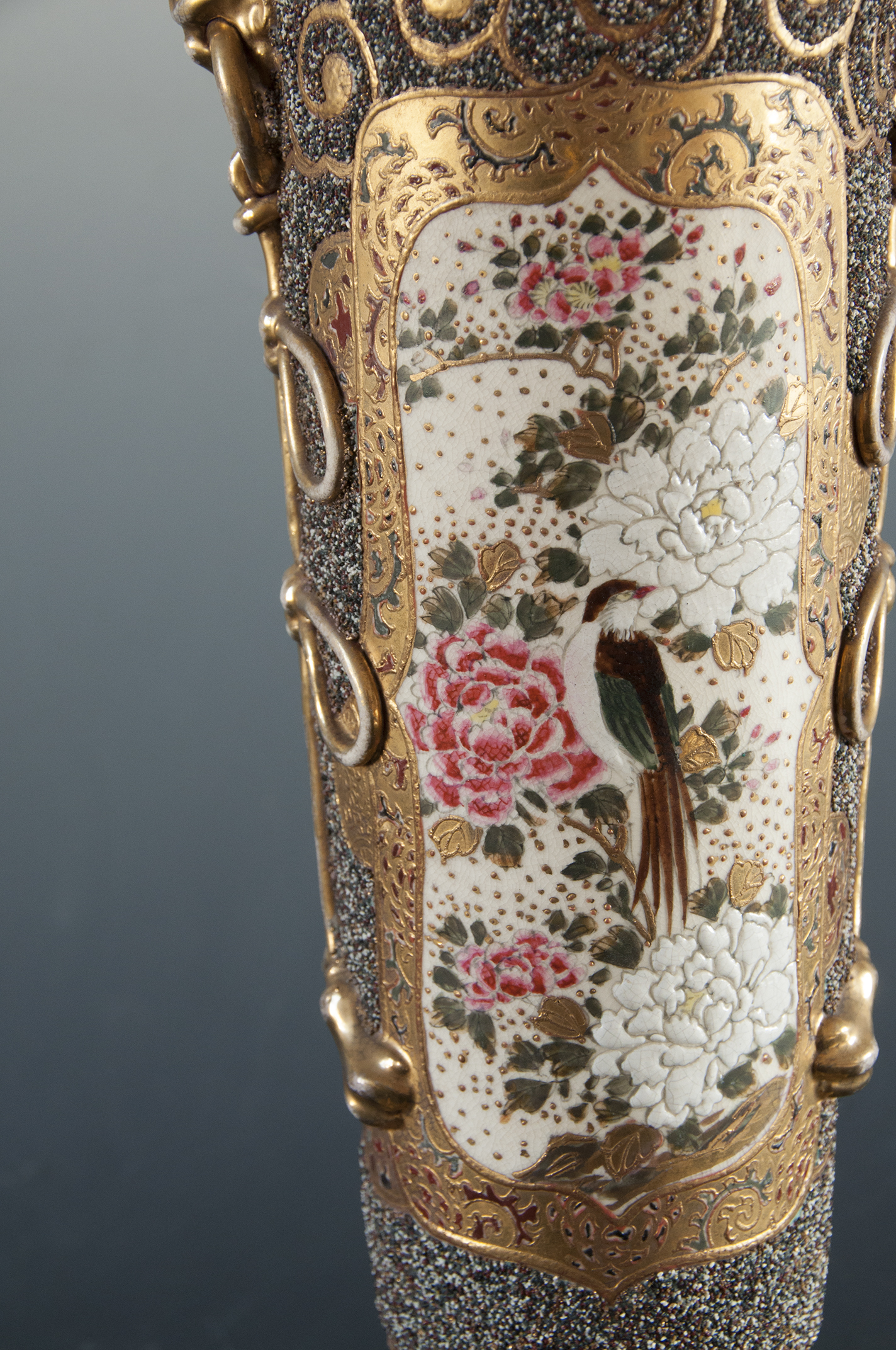 Na ceramicznym korpusie lampy naftowej bogato dekorowana złoceniami przestrzeń, w złotym ornamentem wydzielone pole wpisana dekoracja z kwiatami wiśni, piwonii i sójką.