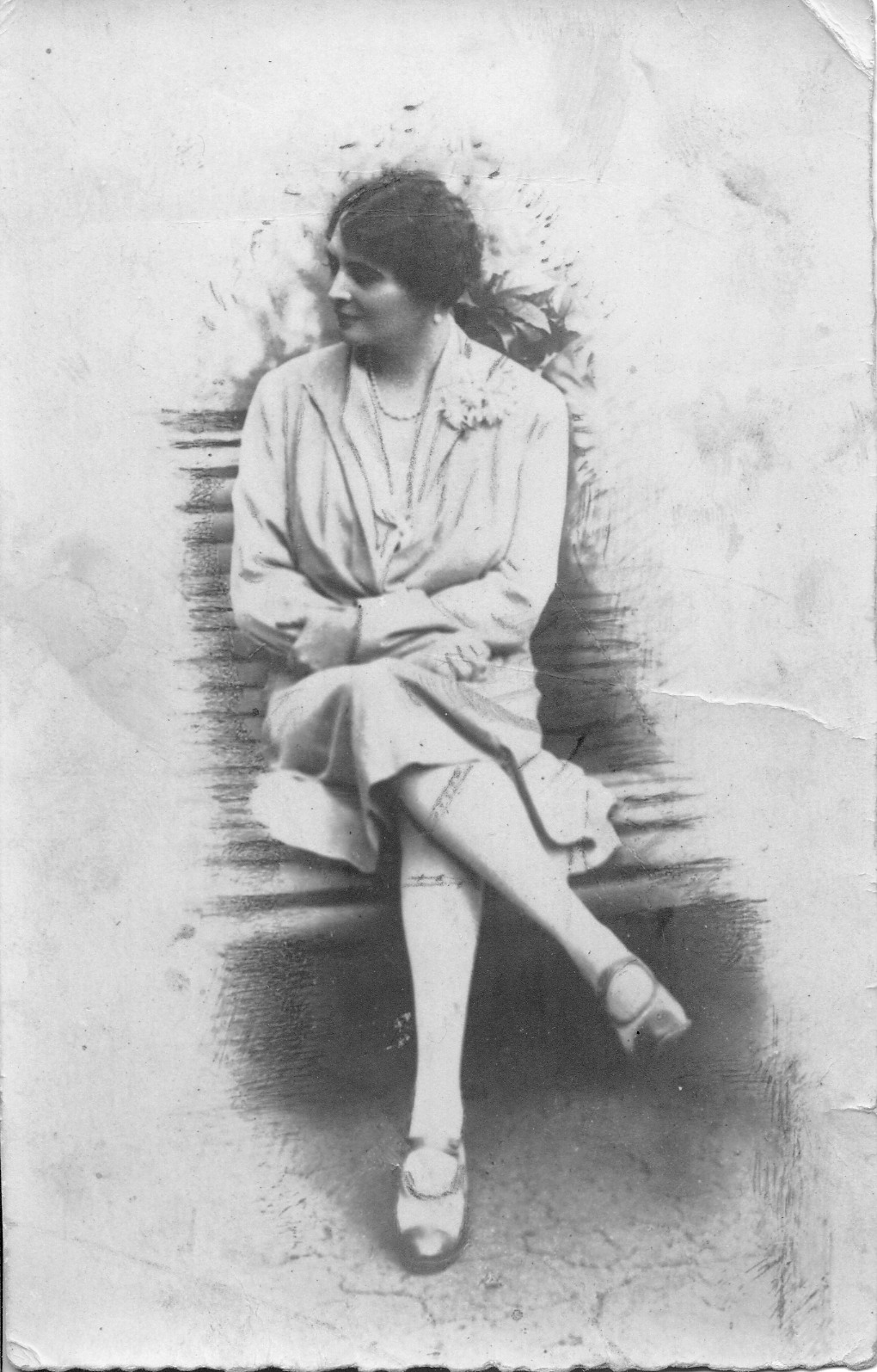 Fotografia archiwalna, czarno-biała, wykonana w latach dwudziestych XX wieku przedstawia Marię Adamową Zamoyską. Kobieta siedzi na ławce, w swobodnej pozie, z głową skierowaną w prawo. Ubrana jest w jasną sukienkę, ozdobioną z lewej strony, przy kołnierzu, kwiatem. Na szyi ma sznur pereł, a w uszach perłowe kolczyki.