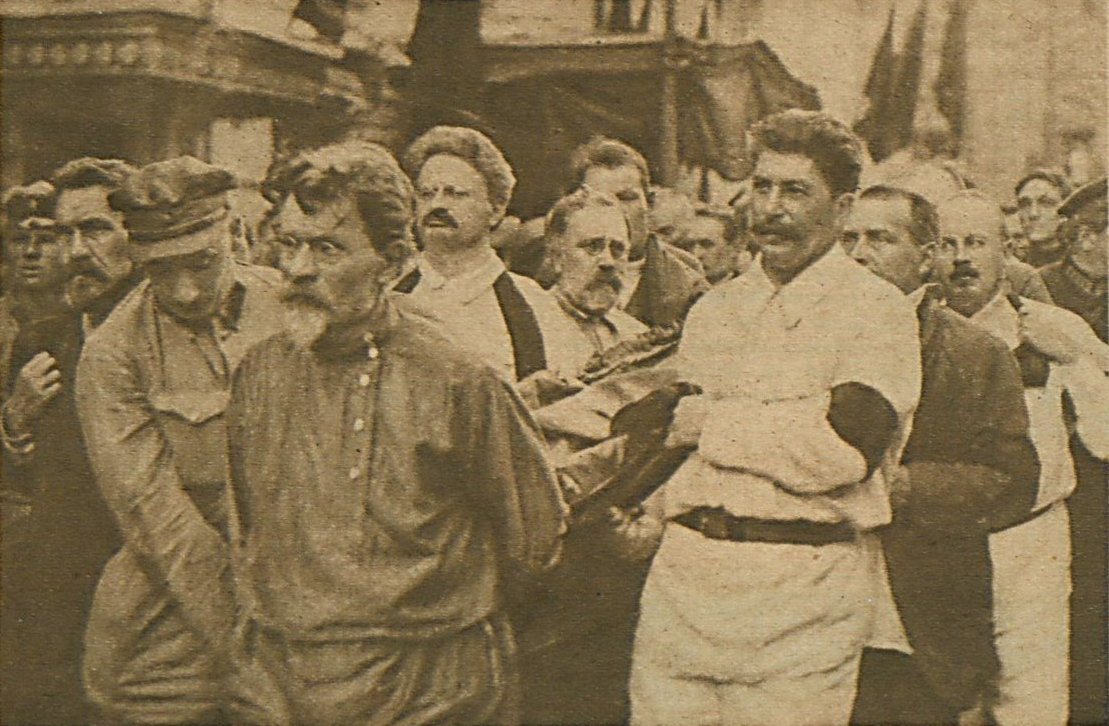 Fotografia archiwalna z 1926 r. przedstawiająca pogrzeb Feliksa Dzierżyńskiego w Moskwie. Przedstawia mężczyzn niosących trumnę, a pierwszym planie ubrany w białą bluzę i spodnie Józef Stalin.