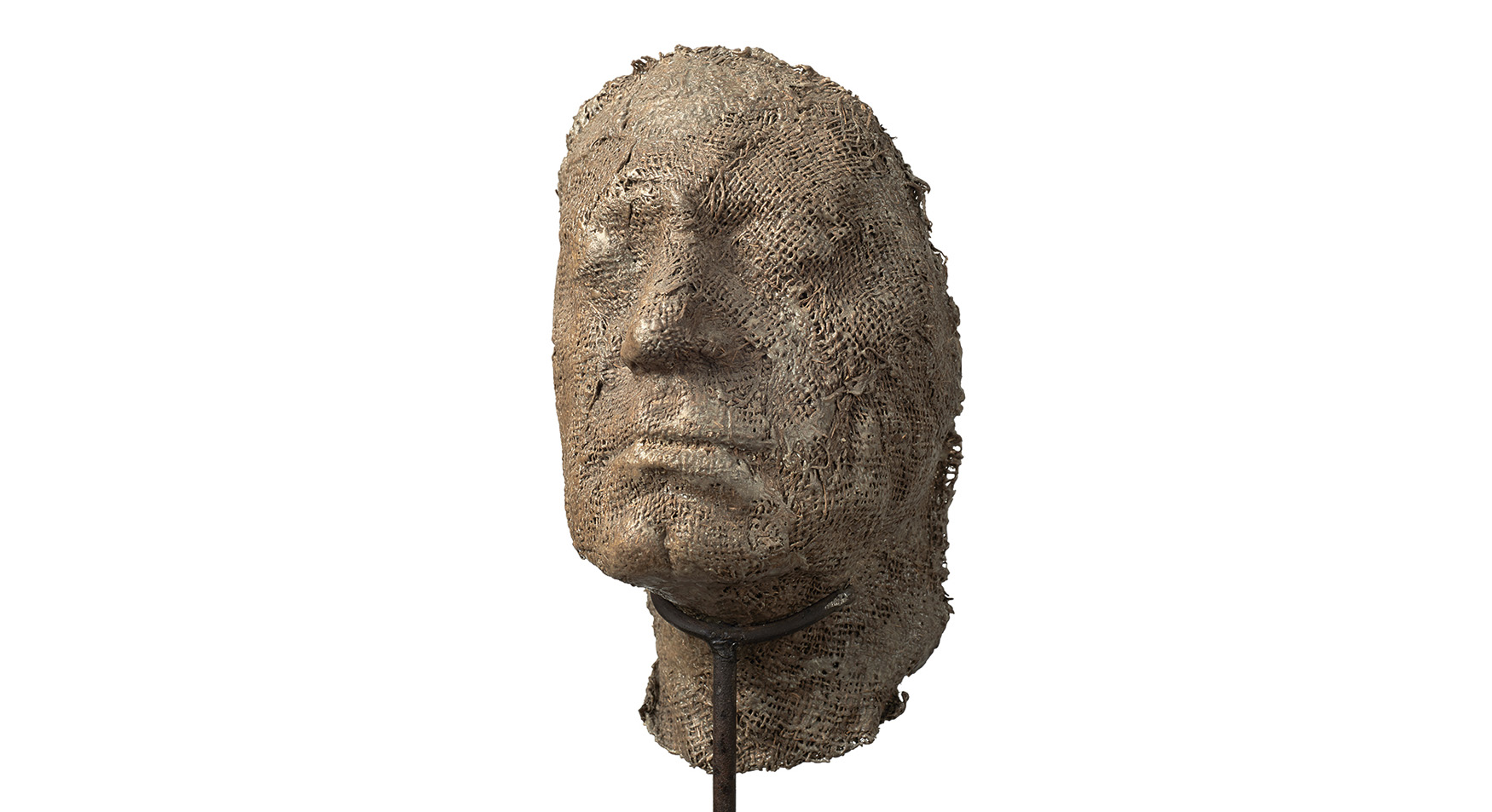 Magdalena Abakanowicz

urodzona w 1930 roku w Falentach – zmarła w 2017 roku w Warszawie

Portret anonimowy 

powstały w 2000 roku

Żywica metal (stelaż) 

wymiary: 103 x 22 x 23

Starak Collection


Praca ukazuje silnie uproszczoną, niemal ascetyczną głowę – rzeźbę wykonaną z żywicy o powierzchni przypominającej spękaną, wyschniętą ziemię. Materiał ten nadaje formie porowatą, kruchą strukturę, która zdaje się być świadectwem upływu czasu, przemijania i organicznej ulotności.


Głowa jest zamocowana na długim, cienkim metalowym pręcie, który osadzony jest w minimalistycznej, kwadratowej podstawie. Ten kontrast między miękką, niemal organiczną materią a zimnym, surowym metalem podkreśla napięcie między cielesnością a abstrakcją, między ludzkim doświadczeniem a mechaniczną formą nośną.


Twarz – pozbawiona większości szyi, jakby wyjęta z ciała i zawieszona w przestrzeni – emanuje głęboką emocją. Zamknięte lub przymknięte oczy otoczone są wyraźnymi bruzdami, które mówią o cierpieniu, melancholii lub intensywnej zadumie. Usta lekko opuszczone podkreślają powagę, a może nawet ból, tworząc wyraz pełen dramatyzmu i skupienia.


Rzeźba zdaje się nie tylko przedstawiać postać, ale raczej wprowadzać widza w przestrzeń emocjonalną, gdzie surowość materiału i minimalizm formy stają się nośnikiem uniwersalnej ludzkiej kondycji.
